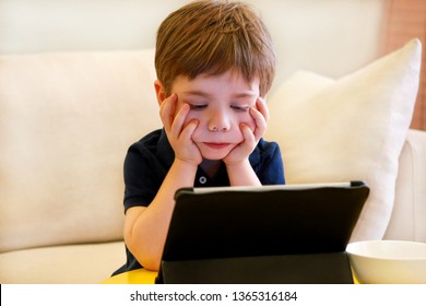 Child using tablet pc on bed at home. Cute boy on sofa is watching cartoon, playing games and learning from laptop. Education, fun, leisure, happiness, modern computer technology and communication. - Shutterstock ID 1365316184