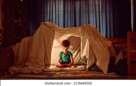 child using tablet pc under blanket at night. Boy with tablet computer in a dark room - Powered by Shutterstock