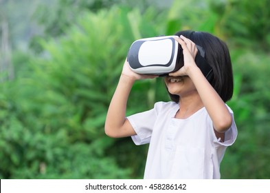 Child With Virtual Reality Headset Sitting Behind Natrue Outdoors At Home.