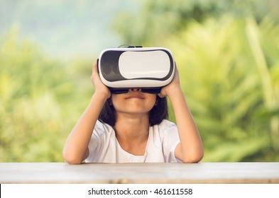 Child With Virtual Reality Headset Sitting Behind Natrue Outdoors At Home.