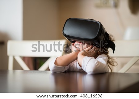 Child with virtual reality headset sitting behind table indoors at home