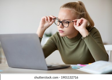 Child Vision Problems And Gadgets Concept. Blonde Teen Girl Fixing Her Glasses While Looking At Laptop Screen, Doing Homework At Home, Using Computer, Having Difficulties With Eyesight, Copy Space