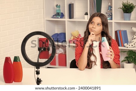 Child vlogger making video blog on phone. Blogging weblog and vlog. Teen girl blogger influencer hold hair conditioner or shampoo bottle recording video for social media.