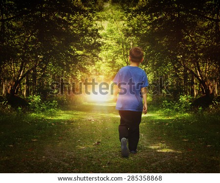 A child is walking in the dark woods into a bright light on a path for a freedom or happiness concept. 