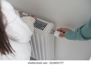 Child warming hands on heating radiator near white wall, closeup