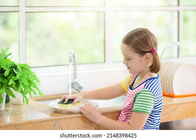 Child washing dishes. Home chores. Kid in white kitchen cleaning plates after lunch at window.