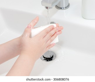 A Child Is Washing Her Hands With A Bar Of Soap.