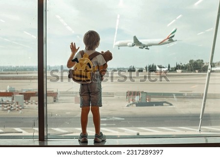 Child, watching from the window of the airport the planes, taking off and landing while waiting at  to board the aircraft for a holiday