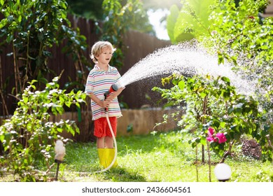 Child watering flowers and plants in garden. Kid with water hose in sunny blooming backyard. Little boy gardening. Summer fun outdoor at home. Family activity in spring. Children help parents. - Powered by Shutterstock