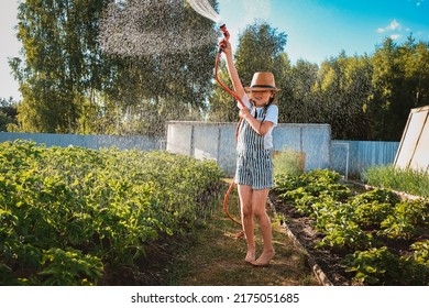 Child watering plants garden. Kid with water hose sunny backyard girl gardening Summer outdoor holidays village. Children Farmer help parents sunset authentic, candid, green living, eco friendly
