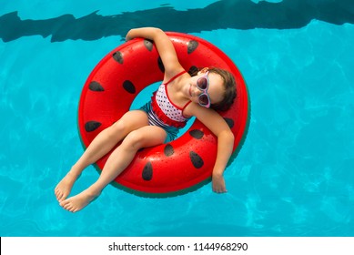 Child with watermelon inflatable ring in swimming pool. Little girl learning to swim in outdoor pool of tropical resort. Hot Summer. Water toys and floats for kids. Healthy sport for children. 