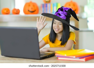 Child Waving And Zooming With Friends Online During Halloween.Asian Girl On Video Call.Daughter Talking To Family Online Zoom.Kid With Costume Using Laptop While Homeschooling.Student At Home.Holidays