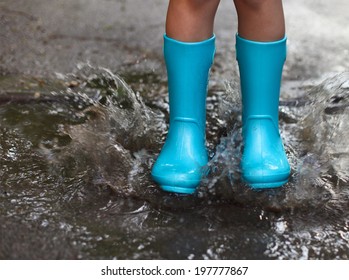 Child Wearing Blue Rain Boots Jumping Into A Puddle. Close Up