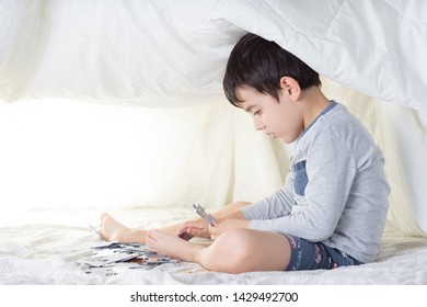 Child Wearing Gray-toned Pajamas In A Makeshift Tent With Bed Sheets Making A Puzzle With White Backgrounds And Soft Lighting