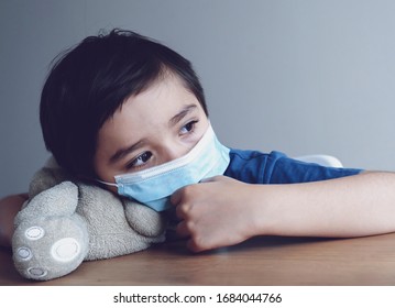 Child wearing medical face mask lying his head on teddy bear with crying tear,Emotional portrait of little boy crying and looking out deep in thought, Protective measures against spreading of Covid-19