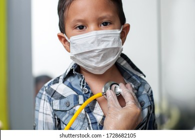 Child Wearing A Medical Mask To Prevent Spread Of Virus Is Getting A Heart Screening With Stethoscope Placed On Chest.