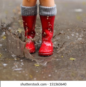 Child Wearing Red Rain Boots Jumping Into A Puddle. Close Up