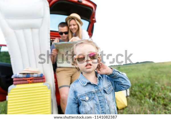 Child wearing\
sunglasses standing on the background of parents with suitcases\
Packed for summer travel