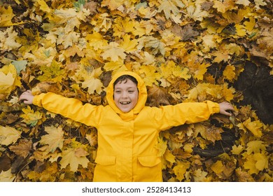 A child wearing a yellow raincoat lies happily among a in golden autumn leaves, smiling and enjoying the crisp fall weather. The leaves create a vibrant backdrop, showcasing the beauty of the season - Powered by Shutterstock