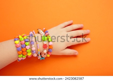 Child wears bracelets on his hands. Kids handmade beaded jewelry on orange background. Top view