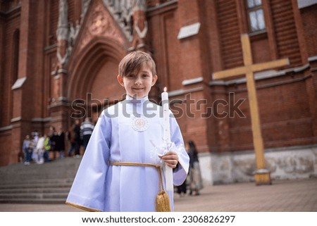 a child in white traditional festive clothes with a saint before his first Eucharist stands near a Catholic church.