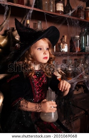 a child witch on Halloween with a flask in his hands looks into the distance in the web and smoke. Brunette girl in a witch costume