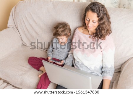 Child and a woman sitting on a sofa watching a laptop and a smart phone.. Technology concept in family.