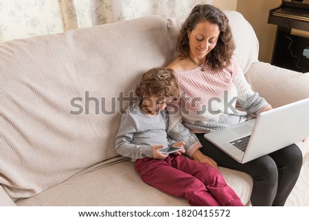 Child and a woman sitting on a sofa watching a laptop and a smart phone.. Technology concept in family.