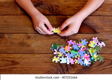 Child Working On Jigsaw Puzzle. Child Holding A Puzzle In Hands. Group Of Jigsaw Puzzles On Wooden Table 