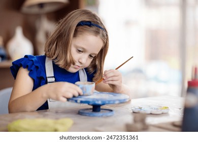 Child working on pottery wheel. Kids arts and crafts class in workshop. Little girl creating cup and bowl of clay. Creative activity for young children in school. Cute kid forming toy with ceramic.  - Powered by Shutterstock