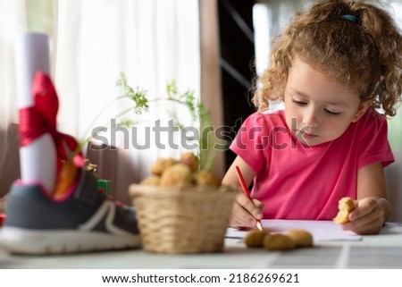 child writing letter on traditional Dutch holiday Sinterklaas in Europe, Netherlands, Belgium. girl put in in boot, shoe carrot for Santa horse, gift, pepernotin chocolate sweet cookies. soft focus