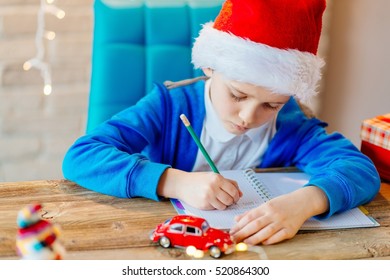 Child Writing A Letter To Santa Claus At Home. Lights Bokeh On Background. Christmas Time