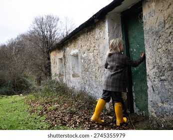 Child in yellow boots exploring rustic stone house in woods