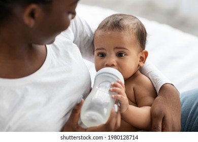 Childcare Concept. Closeup Portrait Of Happy African American Woman Holding Baby Bottle And Feeding Her Cute Little Black With Milk At Home. Nutrition, Love, Care And Family, Babysitting