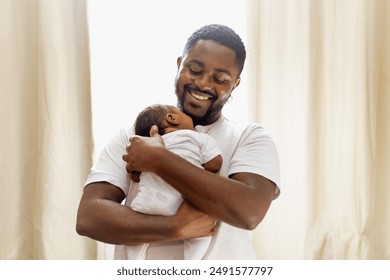 Childcare concept. Happy, smiling and loving african american father giving a hug to his newborn baby daughter at home, young black dad spending time with his cute little daughter, in the living room. - Powered by Shutterstock