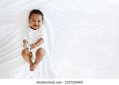 Childcare Concept. Portrait Of Adorable Little Black Baby Lying On Bed With Teether In Hand, Top View Shot Of Cute African American Infant Boy Or Girl Wearing Bodysuit Smiling At Camera, Copy Space - Powered by Shutterstock