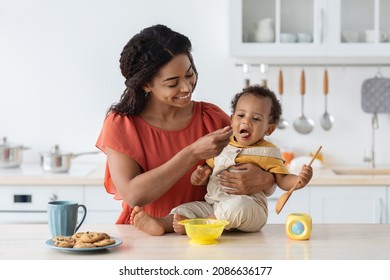 Childcare. Loving Black Mom Feeding Her Cute Baby Son From Spoon In Kitchen, Caring Mother Giving Porridge Or Mash Fruit Puree To Adorable Infant Child At Home, Preparing Healhy Food For Kid - Shutterstock ID 2086636177
