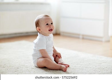 Childhood, Babyhood And People Concept - Happy Little Baby Boy Or Girl Sitting On Floor At Home