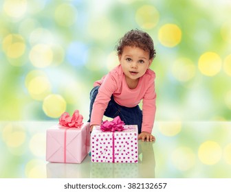 Childhood, Birthday, Holidays And People Concept - Little African American Baby Girl With Gift Boxes And Confetti Crawling On Floor Over Green Summer Holidays Lights Background