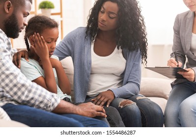 Childhood depression concept. Young black parents and their little daughter sitting at psychologist consultation, mother encouraging girl.
