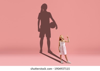 Childhood and dream about big and famous future. Conceptual image with girl and drawned shadow of basketball, soccer female player on coral pink background. Childhood, dreams, education concept. - Shutterstock ID 1904937115