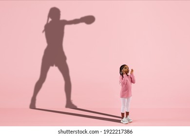 Childhood and dream about big and famous future. Conceptual image with girl and drawned shadow of female boxer on coral pink background. Childhood, dreams, imagination, education concept.