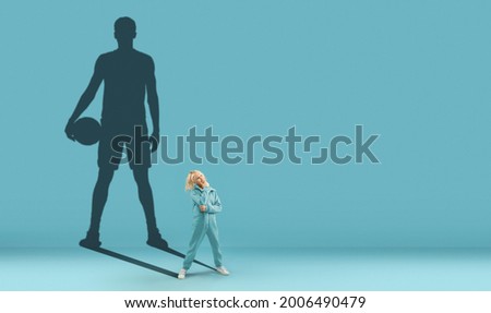 Childhood and dream about big and famous future. Conceptual image with boy and drawned shadow of sportive male basketball player on blue background. Copy space for ad, text.