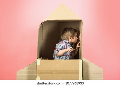 Childhood, Dream, Imagination Concept - Adorable Boy Plays In Astronaut, Looks In Illuminator Cardboard Space Rocket. Kid Plays Home With Cardboard Rocket Ship. He Imagining He Is In Space With Stars.