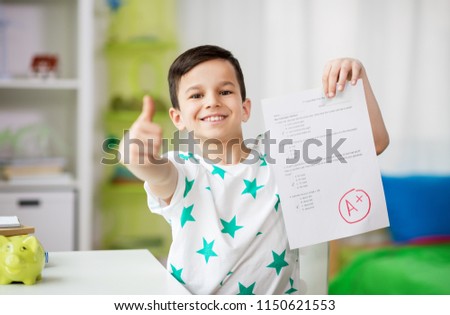 childhood, education and people concept - happy smiling boy holding school test with a grade showing thumbs up