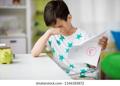 childhood, education and people concept - sad boy holding school test with f grade