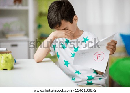 childhood, education and people concept - sad boy holding school test with f grade