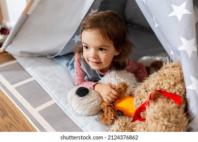 childhood, hygge and people concept - happy little baby girl playing with toys in kid's tent or teepee at home