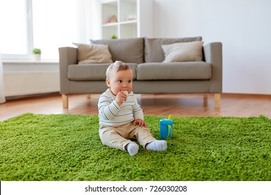 Childhood, Kids And People Concept - Baby Boy Sitting On Floor With Sippy Cup And Eating Rice Cracker At Home