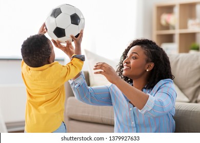 Childhood, Kids And People Concept - Happy African American Mother And Her Baby Son Playing With Soccer Ball Together On Sofa At Home